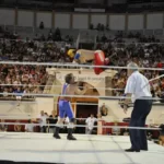 deux catcheurs combattant dans les arènes de Béziers sous le regard de l'arbitre et d'une foule nombreuse